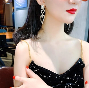 Close-up of elegant long heart drop earrings with white pearls on a female model