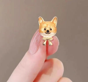 Gros plan d'une boucle d'oreille Corgi en émail orange et blanc tenue entre les doigts