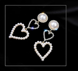 Detail view of gold heart earrings with faux pearls and rhinestones on black silk fabric
