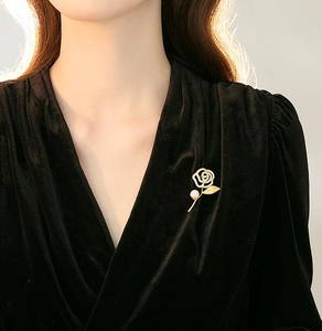 Detail view of a golden rose brooch with pearl on black velvet blazer lapel