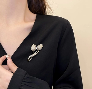 Détail d'une élégante broche tulipe dorée ornée de cristaux sur un revers noir chic