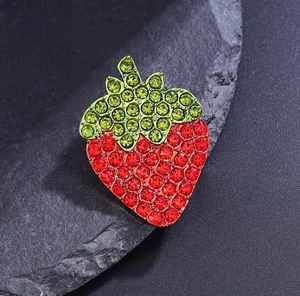 Macro d'une broche fraise avec strass rouges et verts sur fond de roche noire texturée