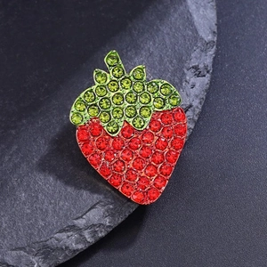 Broche fraise chic avec strass rouges et verts posée sur une pierre naturelle noire