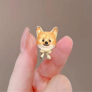 Broche Shiba Inu mignonne en émail avec nœud doré tenue entre les doigts