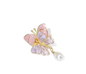 Détail d'une élégante broche papillon en émail rose avec une perle blanche suspendue