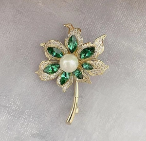 Vue détaillée d'une broche fleur avec cristaux verts, perle blanche et pavé de zircones