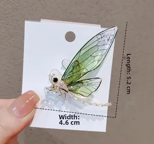 Detailed view of green dragonfly brooch with dimensions 5.2cm x 4.6cm on display card