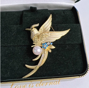 Macro detail of bird brooch with pink pearl and blue enamel flowers in black jewelry box