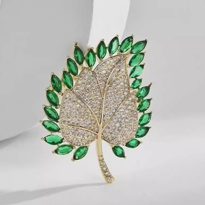 Macro detail of leaf brooch with green marquise gems and white pavé crystals
