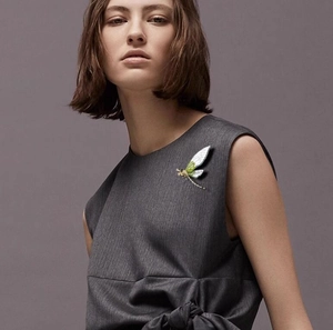 Detailed view of an emerald green cicada brooch pinned on a grey sleeveless top