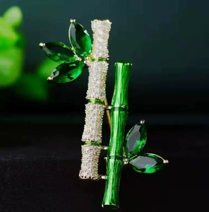Macro detail of a bamboo brooch featuring vibrant green gemstones and enamel craft