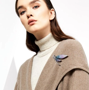 Detailed view of luxury dragonfly brooch with purple gradient wings on a beige sweater