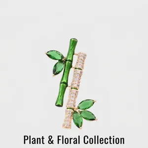 Classical bamboo brooch with green crystals and gold accents on a plain background