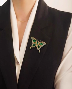 Detailed macro view of the luxury emerald butterfly brooch worn on a black blazer lapel