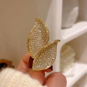 Macro shot of gold leaf brooch with micro-pave crystals on a white knit sweater