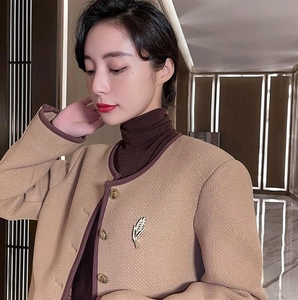 Détail d'une broche épi de blé dorée sertie de cristaux sur un manteau en tweed