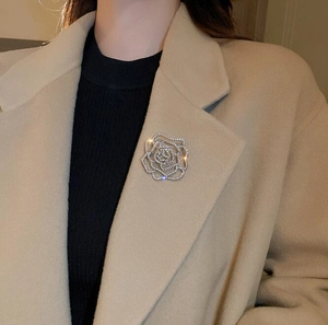 Détail d'une broche fleur en strass portée sur un manteau en laine beige chic