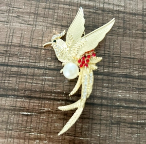 Detail of golden bird brooch with pearls and rhinestones on a wooden background