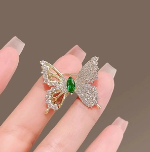 Macro detail of golden butterfly brooch with sparkling zircons and a green marquise stone