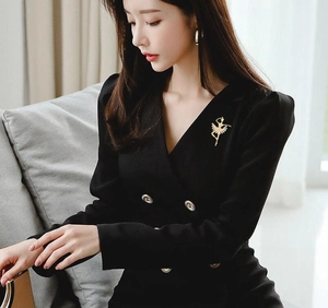 Détail d'une élégante broche ballerine dorée sur un blazer noir à double boutonnage