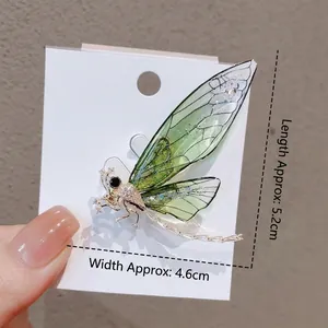 Green dragonfly brooch with sparkling crystals and translucent wings on white card