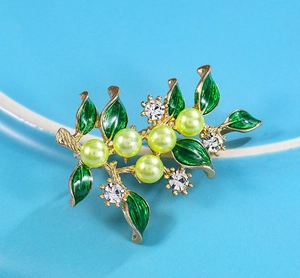 Detailansicht einer goldenen Ast-Brosche mit grünen Emaille-Blättern und Perlen