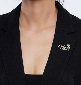 Detail view of a golden Heart letter brooch with cupid angel on a black blazer lapel