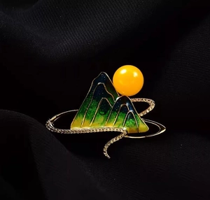 Macro shot of green enamel landscape brooch with yellow pearl on gold plating