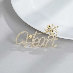 Macro shot of gold Cupid Heart brooch with sparkling zircon inlays on gray surface