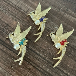 Three elegant gold phoenix bird brooches with pearls and crystals on a wooden background