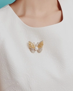 Close-up of a luxury gold butterfly brooch with yellow marquise gems and a large pearl