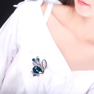 Vintage swan brooch with blue crystals and drop-shaped stone on a white shirt