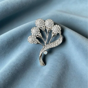 Broche élégante bouquet de fleurs argentées avec strass brillants et détail de pierre bleue