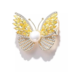 Close-up of luxury gold butterfly brooch with yellow gemstones and white center pearl