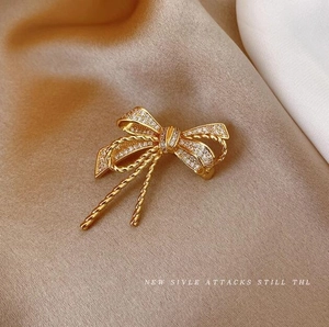 Elegant gold bow brooch with sparkling cubic zirconia on light brown fabric backdrop