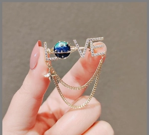 Close-up of silver LOVE brooch with sparkling rhinestones and a blue planet tassel detail