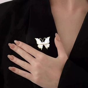 Elegant butterfly brooch in gold and white pearl, worn on a stylish black suit jacket