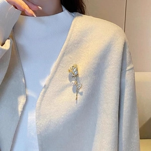 Vue détaillée d'une broche rose dorée avec zircons et perle sur un manteau de laine gris