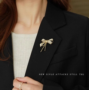 Elegant gold bow brooch with sparkling crystals and tassels on black blazer lapel