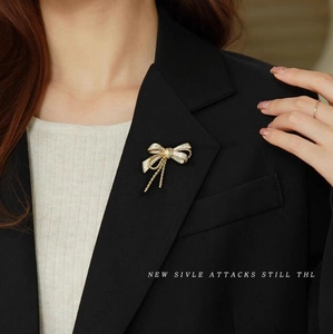 Detail of elegant gold bow brooch with pavé rhinestones and tassels on black suit blazer