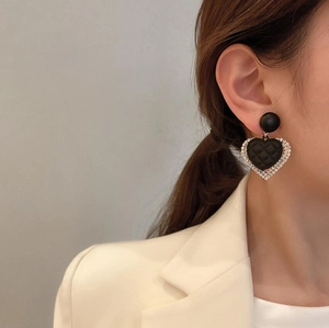 Detail of heart-shaped earring with quilted texture and rhinestones on female model
