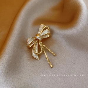 Detail of a golden bow brooch with pavé zircon stones on champagne silk background