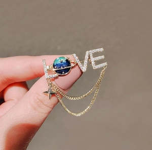 Macro detail of LOVE brooch with blue enamel planet, zircon inlay and tassel chains