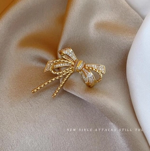 Elegant gold bow brooch with sparkling crystals and metal tassels on silk background