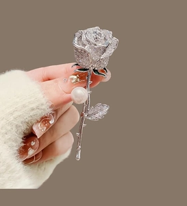 Gros plan d'une broche rose avec cristaux, feuille en émail vert et une grande perle ronde