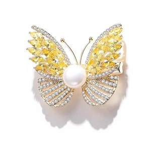 Elegant luxury butterfly brooch with yellow gemstones and a large white pearl in gold finish