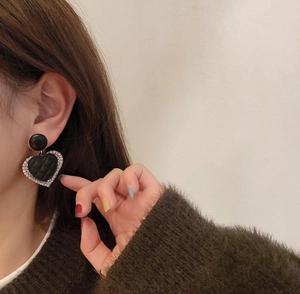 Close-up of heart earrings with quilted texture and silver rhinestones on a female model