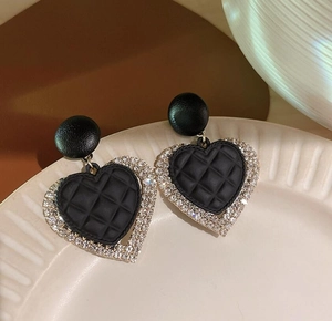Detailed close-up of heart-shaped black quilted earrings with sparkling crystal border