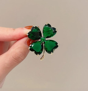 Macro view of a gold clover brooch with heart-cut emerald green crystals and claw setting
