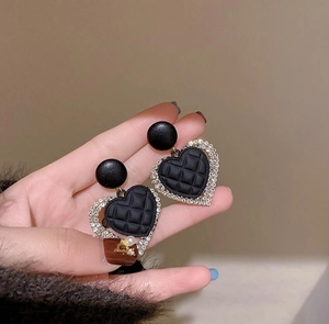 Detailed view of heart-shaped earrings with black quilted pattern and sparkling zircon crystals